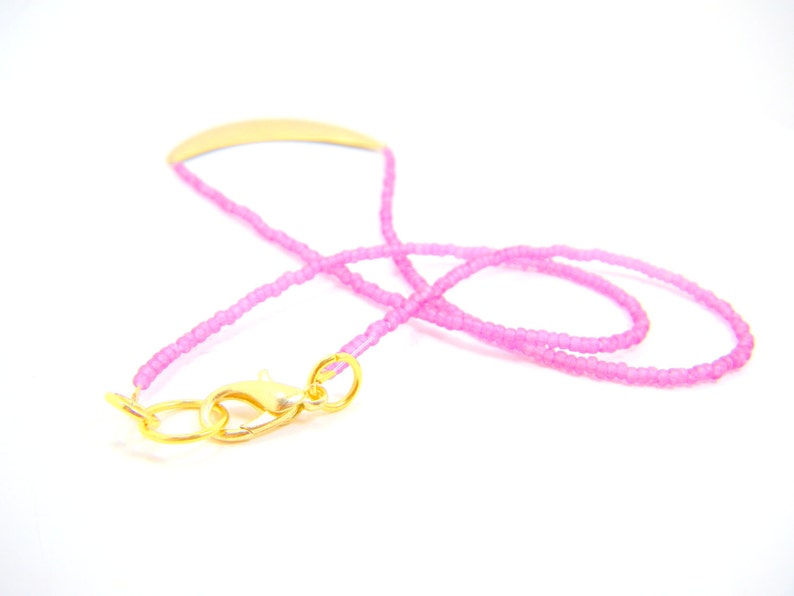 May include: A pink beaded necklace with a gold clasp. The necklace is made of small, round beads and has a simple, elegant design.