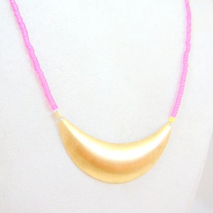 May include: A gold crescent moon pendant necklace with a pink beaded chain.