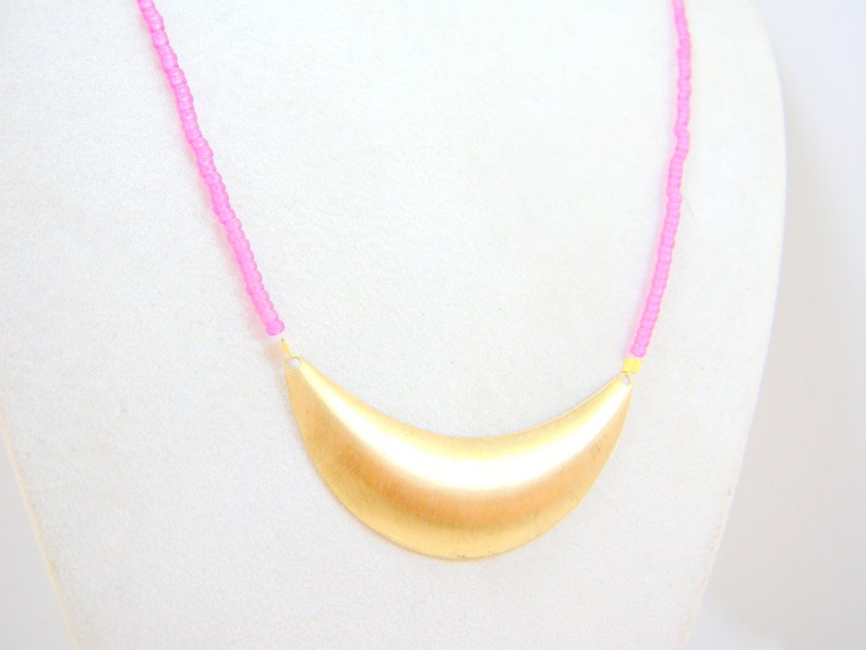 May include: A gold crescent moon pendant necklace with a pink beaded chain.