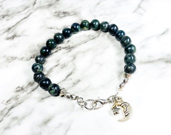May include: A dark green gemstone bracelet with a silver chain and a silver charm of a crescent moon and a star.