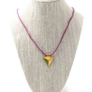 May include: A pink beaded necklace with a gold triangular pendant. The pendant has a green center.