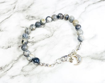 May include: A gray and white stone beaded bracelet with a silver clasp and a silver charm of a crescent moon and a star.