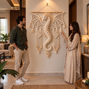 Può includere: Un grande arazzo in macramè color bianco sporco a forma di drago, caratterizzato da ali ampie e dettagliate e da una lunga coda arricciata. L'opera è appesa a un bastone di legno e presenta nappe decorative e motivi a nodi geometrici.