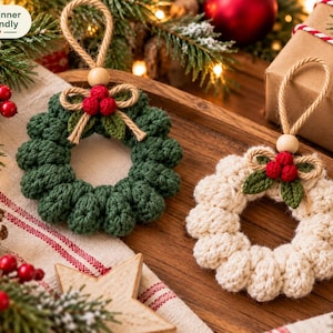 May include: Two round crochet ornaments, one dark green and one cream, each featuring a small jute rope hanger, a wooden bead, and a decorative cluster of three red crocheted berries with two green crocheted leaves tied with a jute bow.
