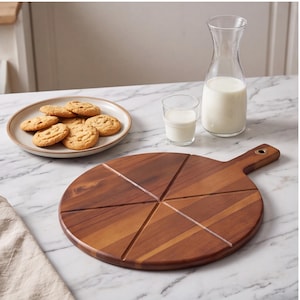 May include: A round wooden serving board with a handle and pre-cut grooves in a star pattern, positioned next to a ceramic plate filled with round cookies, a small glass of milk, and a clear glass carafe filled with white milk.