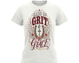 May include: A white short-sleeved t-shirt featuring a central graphic with the text MADE OF GRIT & GRACE. The design includes a brown horseshoe, a black cross, pink flowers, green foliage, and a light pink bow, all framed by decorative swirls.