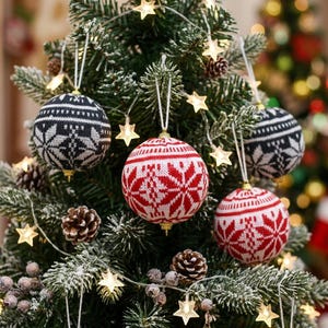 Könnte beinhalten: Vier kugelförmige Weihnachtsanhänger mit einer gestrickten Textur und einem Fair-Isle-Schneeflockenmuster. Zwei Anhänger sind schwarz-weiß, zwei sind rot-weiß. Jede Kugel hängt an einer weißen Schnur und hat eine goldfarbene Kappe am Boden.
