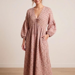 May include: A dusty pink midi dress featuring a small dark floral print, a deep V-neckline with a tie closure, long voluminous sleeves with gathered cuffs, and side pockets. The fabric has a textured, crinkled appearance throughout the garment.