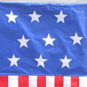 May include: A blue flag with 13 white stars and 13 red and white stripes. The flag is made of a thin, lightweight material.