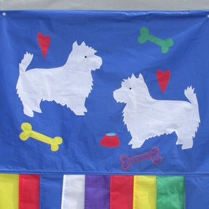 May include: A blue fabric banner with two white felt dog silhouettes, red hearts, yellow and green bone shapes, and a red food bowl. The banner has a fringe of yellow, red, blue, white, purple, yellow, green, and blue fabric.