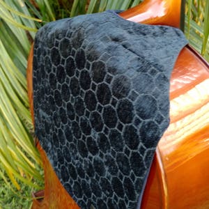 May include: A dark blue bass clef bib with a geometric pattern, draped over a wooden upright bass. The bib has a tag that reads "Bass Clef Bib". The bass has a glossy finish.