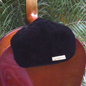 May include: A black velvet cello endpin rest with the text "cellobib.com" on it. The rest is attached to a brown cello.