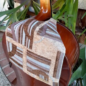May include: A brown cello with a beige and brown patterned fabric cover over the back. The fabric has a geometric design with stripes and squares.