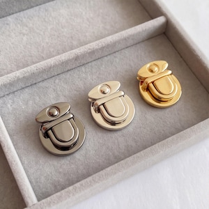 May include: Three round metal twist locks for bags or purses, featuring a smooth, polished finish. The set includes one dark gunmetal, one silver-tone, and one gold-tone closure, each with a central rotating latch mechanism and a top stud.