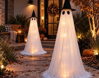 May include: Two tall, cone-shaped ghost decorations standing on a gravel path. Each ghost is draped in sheer white fabric, illuminated from within by warm lights, and topped with a pointed black witch hat featuring two oval black eye cutouts.