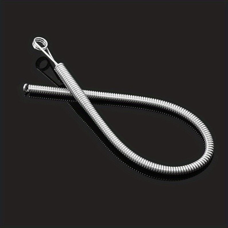 May include: A flexible silver-colored metal spring tool with a tightly coiled body and a small circular loop at one end. The tool is bent into a curved shape, showcasing its metallic texture and uniform coil pattern throughout its entire length.