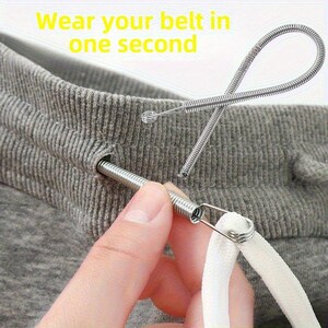 May include: A silver metal spring-style drawstring threader tool with a looped end, shown inserting a white cord into the waistband of grey fabric. The text "Wear your belt in one second" is printed in yellow at the top of the image.