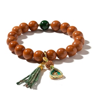 May include: A beaded bracelet featuring smooth, glossy brown spherical beads, a single dark green bead, and a gold-toned charm attachment. The charm includes a small green triangular pendant, a textured brown bead, and a green fabric tassel.