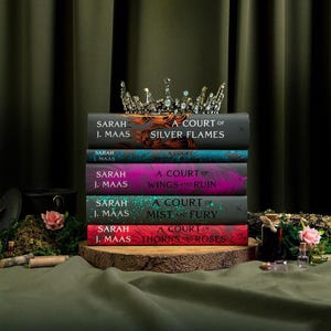 May include: A stack of five books by Sarah J. Maas titled A Court of Silver Flames, A Court of Frost and Starlight, A Court of Wings and Ruin, A Court of Mist and Fury, and A Court of Thorns and Roses, topped with a silver metal crown.