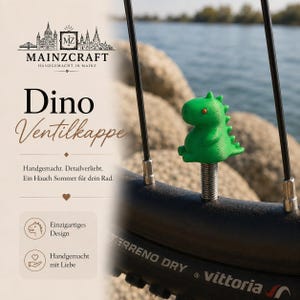 Könnte beinhalten: Eine leuchtend grüne, dinosaurierförmige Ventilkappe, die auf dem Ventil eines Fahrradreifens sitzt. Die kleine, dreidimensionale Figur hat eine texturierte Oberfläche, einen runden Kopf, einen stacheligen Rücken und winzige orangefarbene Augen.