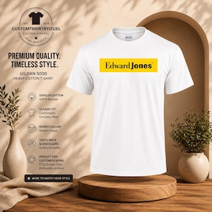 Op de afbeelding: Een wit t-shirt met korte mouwen en een ronde hals, voorzien van een rechthoekige gele afbeelding op de borst met de zwarte tekst Edward Jones. Het shirt is gemaakt van zwaar katoen en heeft een geribbelde kraag en verstevigde nek- en schoudernaden.