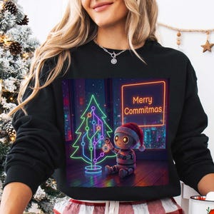 Può includere: Una felpa nera a maniche lunghe con una stampa grafica di un piccolo robot con un cappello da Babbo Natale, seduto accanto a un albero di Natale in stile neon e un cartello con la scritta Merry Commitmas in arancione.