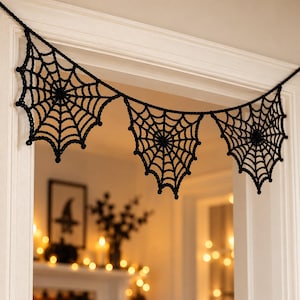 May include: A black crocheted garland featuring three interconnected spider web motifs. The yarn is worked into a detailed radial web pattern with small knots at the points of the web, suspended horizontally across a white door frame.