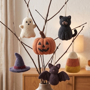 Könnte beinhalten: Ein Set aus sechs gefilzten Halloween-Anhängern an kahlen Zweigen, bestehend aus einem weißen Geist, einem orangefarbenen Kürbis, einer schwarzen Katze, einem violetten Hexenhut, einer dunkelvioletten Fledermaus und einem dreifarbigen Zuckermais.
