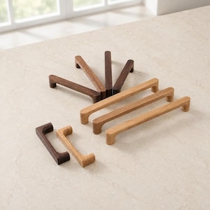 May include: A collection of wooden cabinet pulls in various lengths and wood tones, including dark walnut and light oak finishes. The hardware features a simple, linear design with rounded edges and two mounting points on each handle.