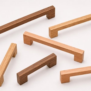 May include: A collection of six rectangular wooden cabinet pulls in varying lengths and wood tones, ranging from light tan to dark brown. Each handle features a straight, linear design with two perpendicular mounting posts at the ends.