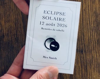 May include: A rectangular white card with a thin black border featuring the text ECLIPSE SOLAIRE, 12 août 2026, Remèdes de rebelle, and Mrs Smith. Below the text is a graphic illustration of a black solar eclipse against a white background.