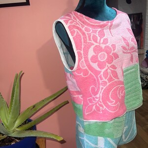 Pode incluir: Um conjunto de top sem mangas e calções feito de tecido turco. O top apresenta um padrão floral cor-de-rosa sobre um fundo branco com um painel verde. Os calções são azul-claros e verdes com um padrão geométrico branco e acabamento.