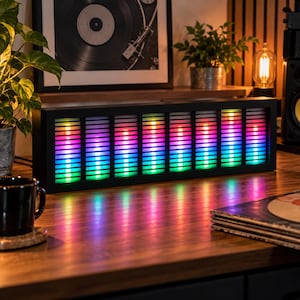 Könnte beinhalten: Ein rechteckiger schwarzer Audiospektrum-Analysator mit acht vertikalen LED-Lichtleisten, die einen Farbverlauf von Grün unten bis Blau, Violett und Rot oben anzeigen, untergebracht in einem schlanken Rahmen und mit einem lebendigen Leuchten.