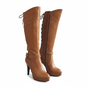 May include: A pair of knee-high tan boots featuring a high stiletto heel, a platform sole, and a side zipper closure. The boots include a decorative strap with a buckle at the ankle and a lace-up detail at the back with light-colored stitching.