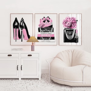 Può includere: Un set di tre stampe artistiche da parete incorniciate con illustrazioni a tema moda. La prima stampa mostra tacchi alti neri con suole rosa, la seconda una pila di libri con un fiocco rosa e perle, e la terza un flacone di profumo con rose rosa.