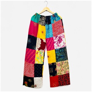 Puede incluir: Pantalones de pierna ancha con un diseño de patchwork vibrante compuesto por varios cuadrados de tela. Los patrones incluyen motivos florales, plumas de pavo real, rayas y estampados animales en colores como amarillo, rosa, rojo, azul y negro.