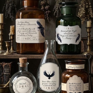 May include: Five glass apothecary bottles with labels featuring raven illustrations and moon phase icons. The collection includes amber and green jars, a clear round bottle, and a teardrop-shaped bottle, all displaying handwritten-style text labels.