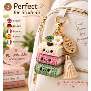 May include: A crochet keychain featuring a stack of three small books with smiling faces, a white flower, a green leaf, a wooden charm engraved with "Good Books Brighter Days," and a cream-colored tassel, all attached to a gold-toned metal clasp.