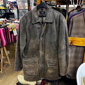 May include: A brown leather jacket with a classic design. The jacket features a collared neckline, a zipper closure, and buttoned pockets. The jacket has a distressed look and is hanging on a black hanger.