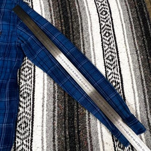 May include: A blue plaid long-sleeve shirt with a ruler laid across it. The shirt has a classic button-down design. The ruler shows measurements from 17 to 72 inches.