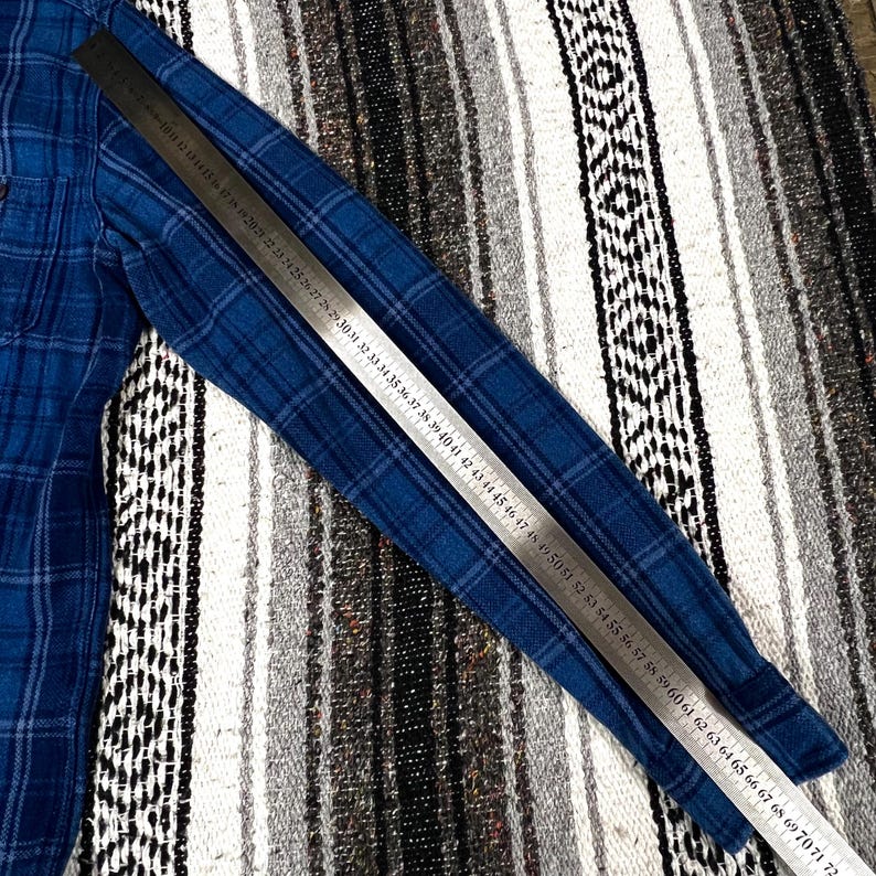 May include: A blue plaid long-sleeve shirt with a ruler laid across it. The shirt has a classic button-down design. The ruler shows measurements from 17 to 72 inches.