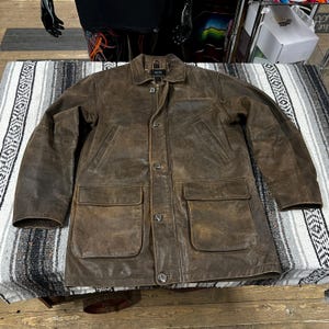 May include: A brown leather jacket with a button-up front, two chest pockets, and two lower pockets. The jacket has a collar and a zipper closure. The leather has a distressed appearance.