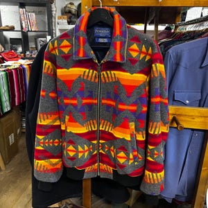 May include: A grey zip-up jacket with a vibrant geometric pattern in red, orange, yellow, and purple. The jacket features a black collar and cuffs, and a Pendleton label.