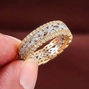 May include: A two-tone ring featuring a central band of silver-colored metal with an intricate floral filigree pattern encrusted with small clear stones, bordered by two outer bands of yellow gold-colored metal set with tiny clear stones.