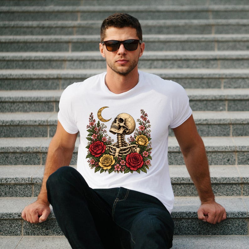 May include: A white short-sleeved t-shirt featuring a graphic print of a human skull and ribcage surrounded by red and yellow roses and a crescent moon. The design is centered on the chest of the garment, which is worn with dark blue jeans.