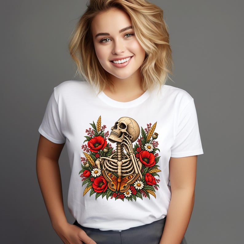 May include: A white short-sleeved t-shirt featuring a graphic print of a human skeleton resting its chin on its hand, surrounded by red poppy flowers, white daisies, green foliage, stalks of wheat, and a large orange and brown butterfly.