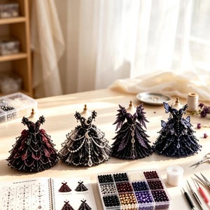 May include: Four miniature dress forms displayed on a table, each wearing a detailed gown. The dresses feature intricate beadwork, lace, and layered fabric in shades of deep red, black, purple, and dark blue, with embellishments like moons.