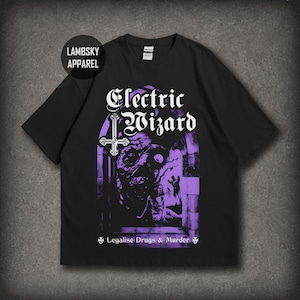 May include: A black short-sleeve t-shirt featuring a purple and white graphic print. The design includes the text Electric Wizard, an inverted cross, a dark figure, and the text Legalise Drugs & Murder. A circular logo reads LAMBSKY APPAREL.
