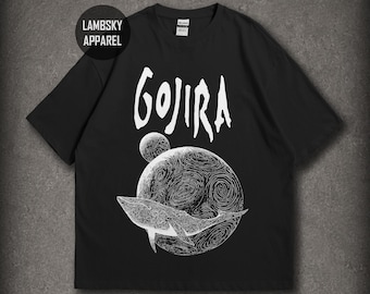 Könnte beinhalten: Ein schwarzes T-Shirt mit kurzen Ärmeln und einem weißen Grafikdruck eines Wals, der vor einem großen Planeten und einem kleineren Mond schwimmt. Der Text GOJIRA ist in einer stilisierten weißen Schrift darüber gedruckt, inklusive LAMBSKY APPAREL.