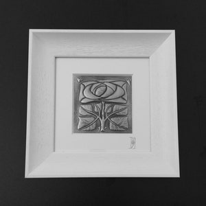 May include: A framed, monochrome artwork with a stylized rose design. The square artwork features a central rose motif and leaf details. It is set within a white wooden frame, creating a clean, minimalist aesthetic.